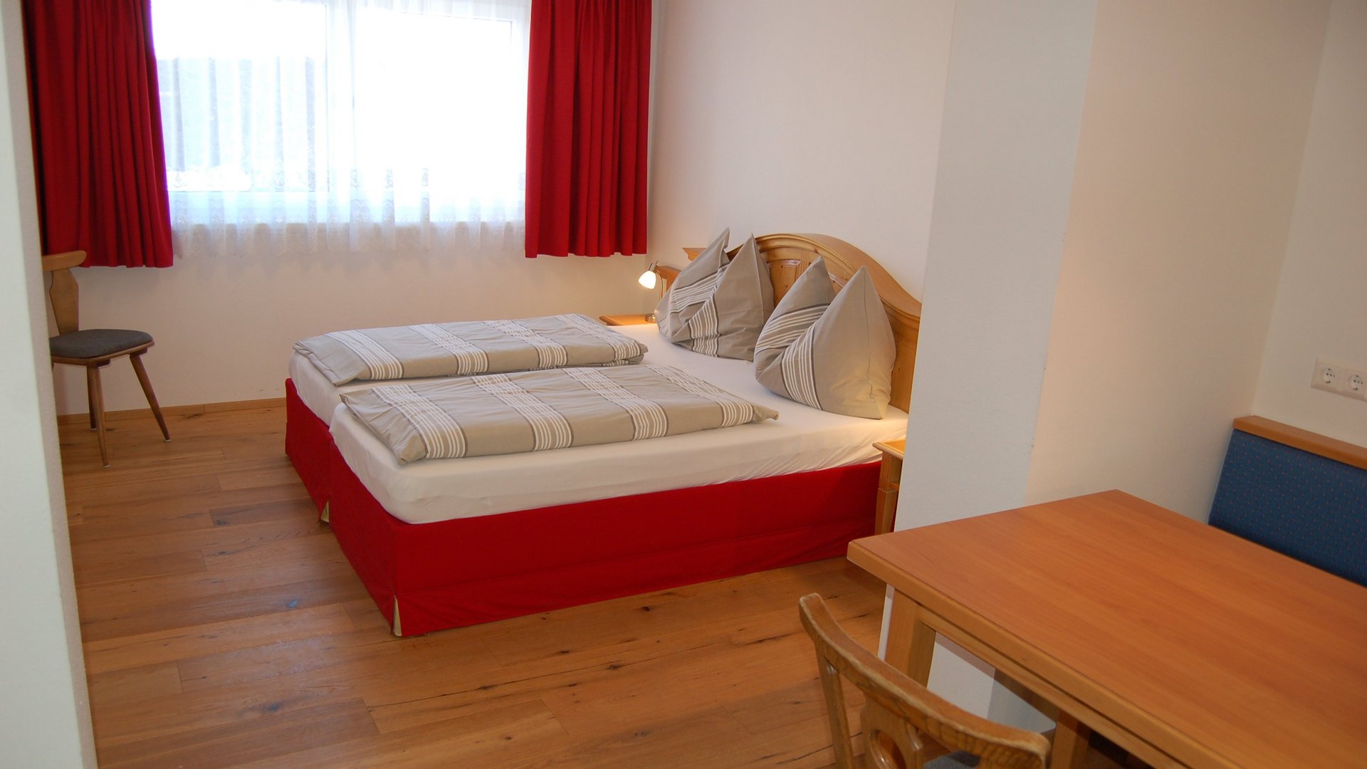Hotelzimmer mit zwei Betten, Holztisch und Fenster mit roten Vorhängen in einem modernen Design.