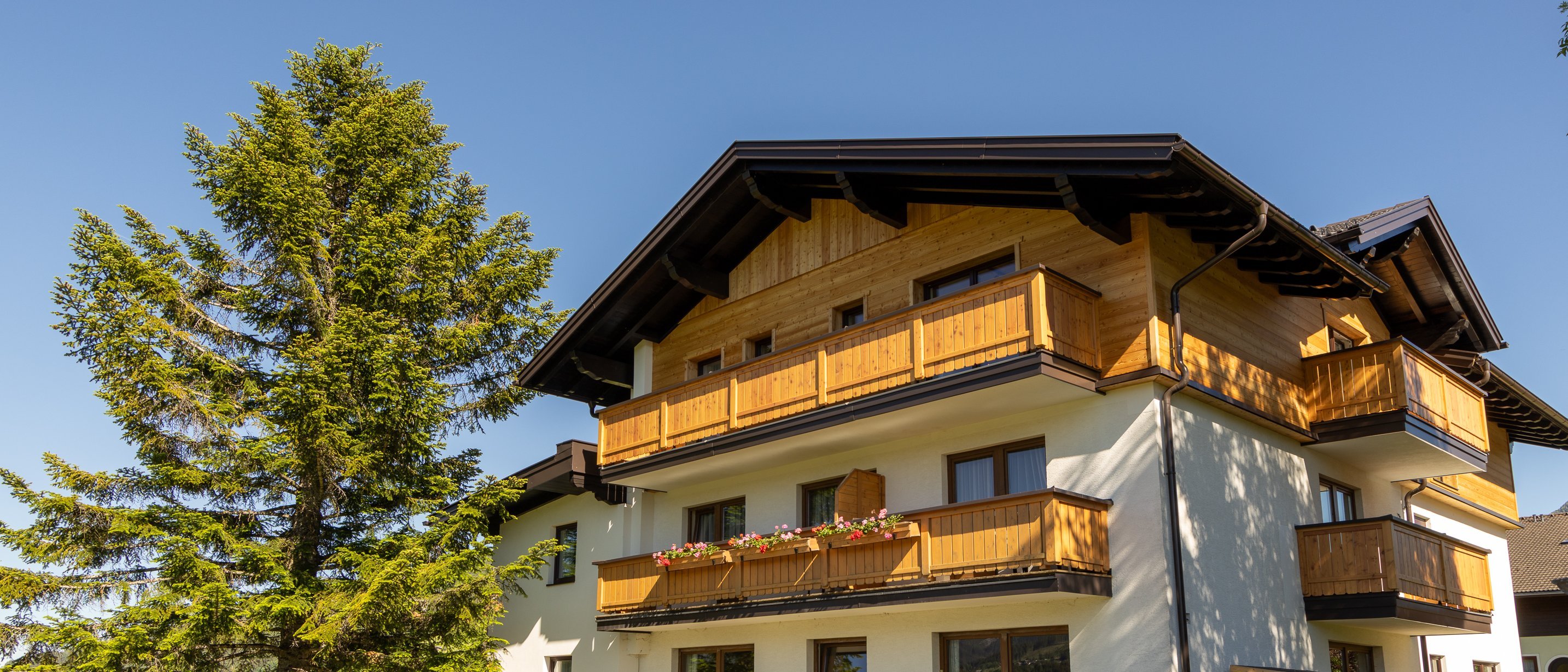 Mehrstöckiges Haus mit Holzbalkonen und einem gepflegten Garten unter klarem Himmel