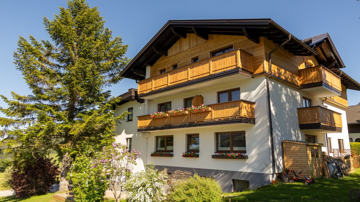 Multi-story house with wooden balconies set in a green landscape under a blue sky