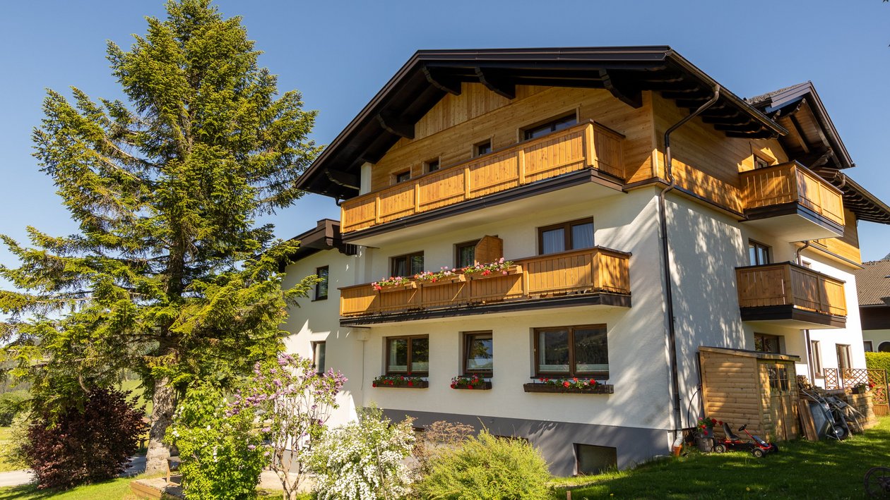 Mehrstöckiges Haus mit Holzbalkonen und einem gepflegten Garten unter klarem Himmel