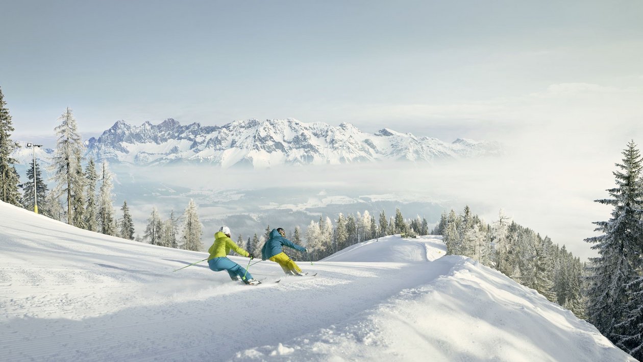 Skifahren in traumhafter Berglandschaft Zwei Skifahrer fahren eine verschneite Piste mit Bergen im Hintergrund hinunter.