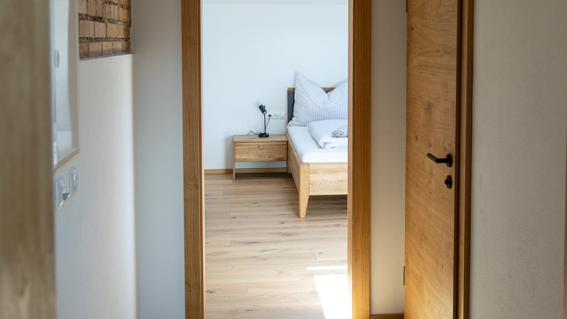 Modernes Design im Eingangsbereich Heller Flur mit Holzboden und einer Tür, die in ein Schlafzimmer führt, beleuchtet von natürlichem Licht.