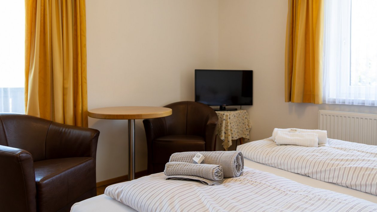 Gemütlicher Rückzugsort Hotelzimmer mit zwei Betten, kleinem Tisch, zwei Stühlen und Fernseher im Innenraum.