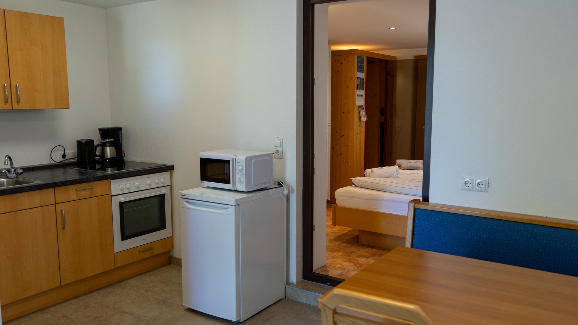 Küchenzeile mit Holzschränken, Kühlschrank, Mikrowelle und Esstisch in einem Apartment.