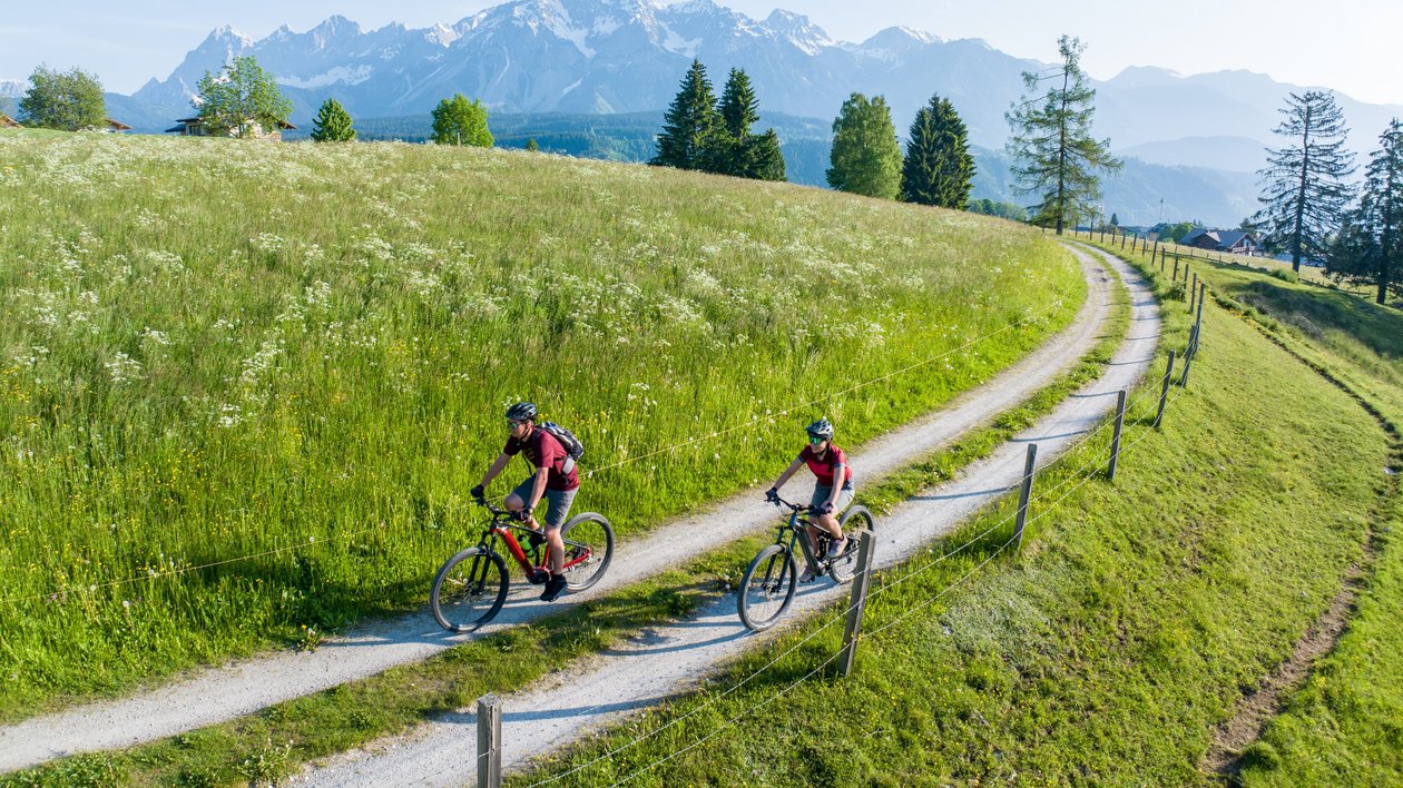 Mountain Biking Adventure Two cyclists riding bikes on a winding path in a green landscape with mountains behind them