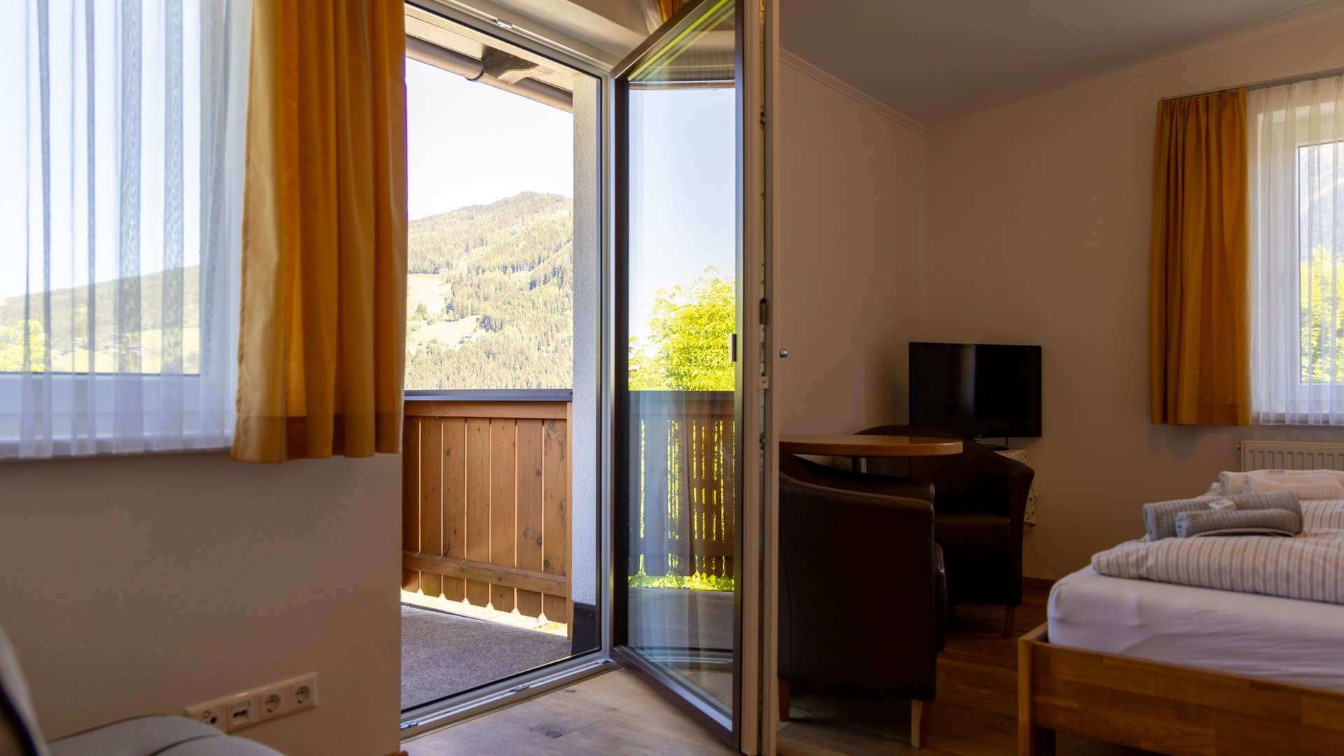 Elegante Unterkunft mit Bergblick Hotelzimmer mit offener Balkontür und Blick auf die Berge, helle Innenausstattung und Sitzbereich