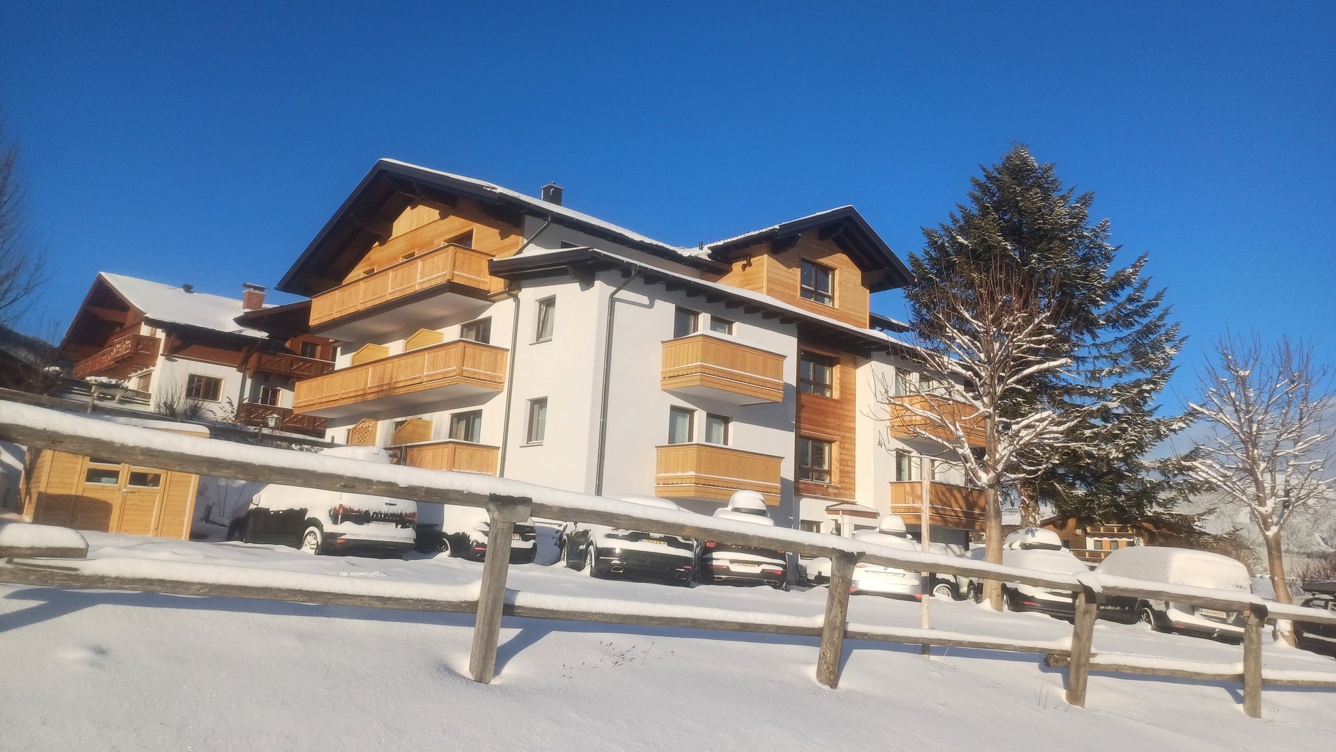 Holzverkleidetes Wohngebäude mit Balkonen und Schnee umgeben unter blauem Himmel