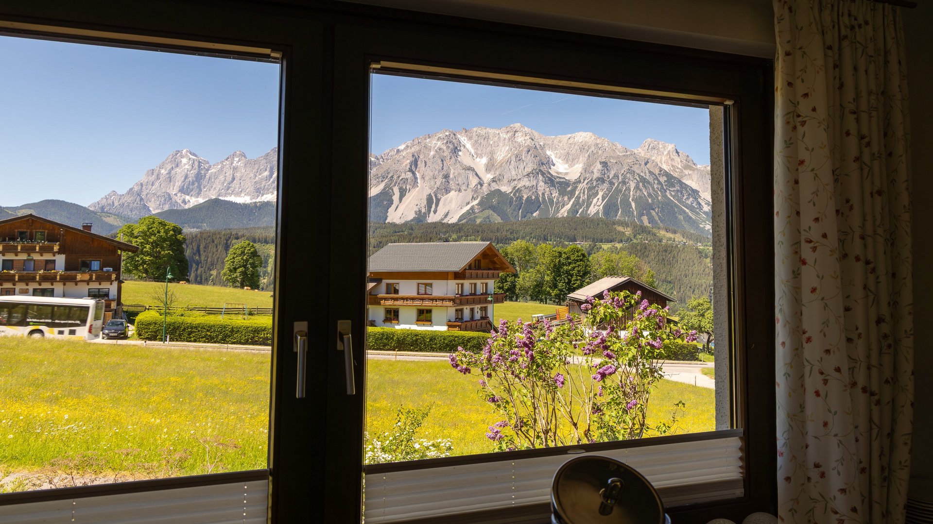 Breathtaking Alpine Vista Window view of mountains with a hotel and flowering plants in foreground under bright sky
