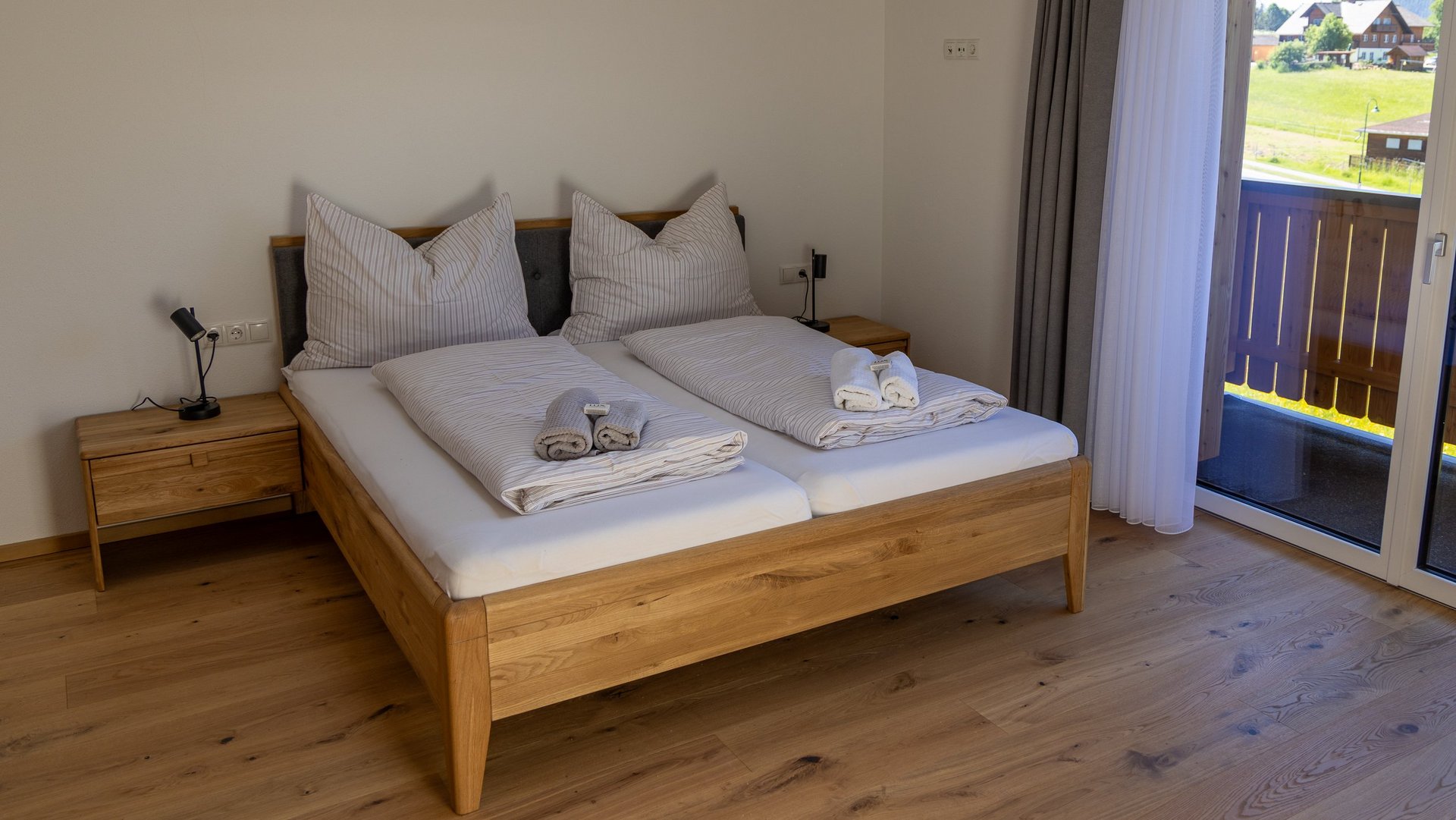 Bright hotel bedroom featuring a double bed, wooden furniture, and balcony access to an outdoor view