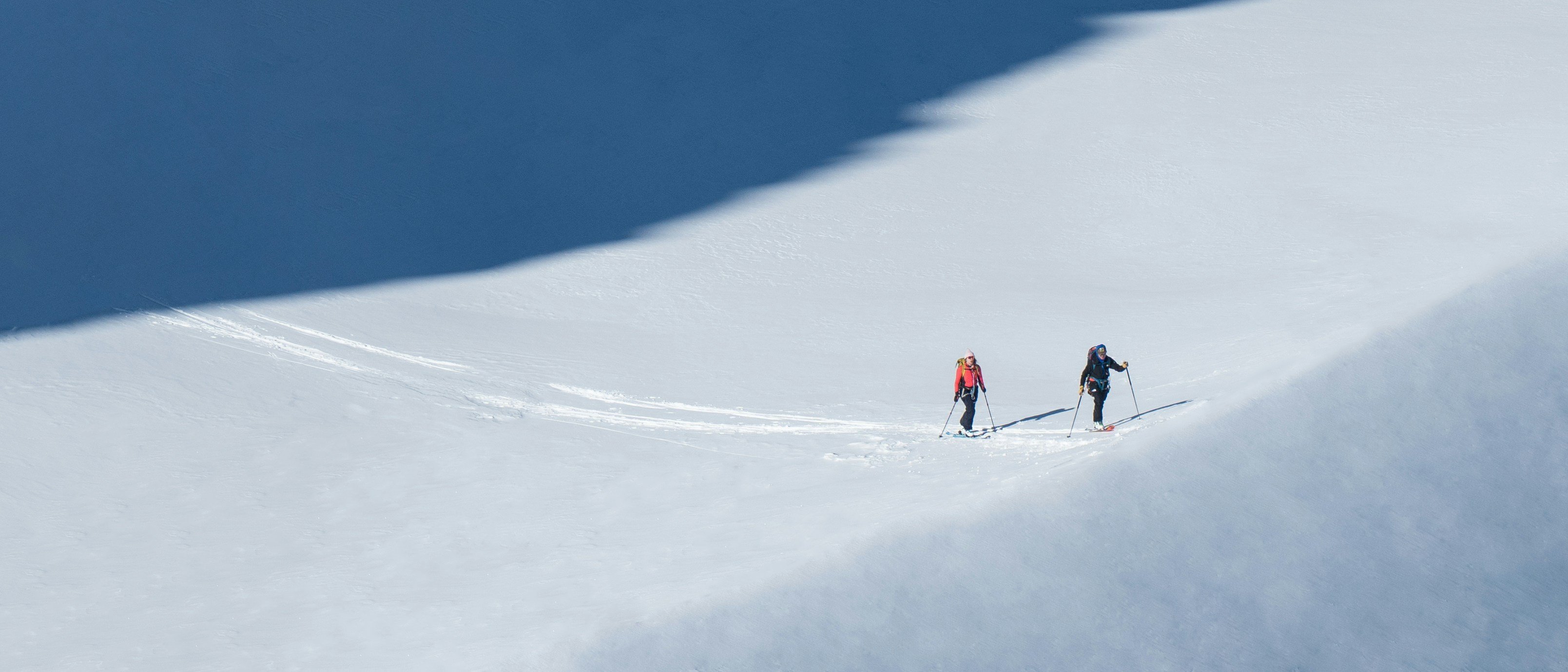 Two skiers navigate a snowy landscape under varying light and shadow conditions.