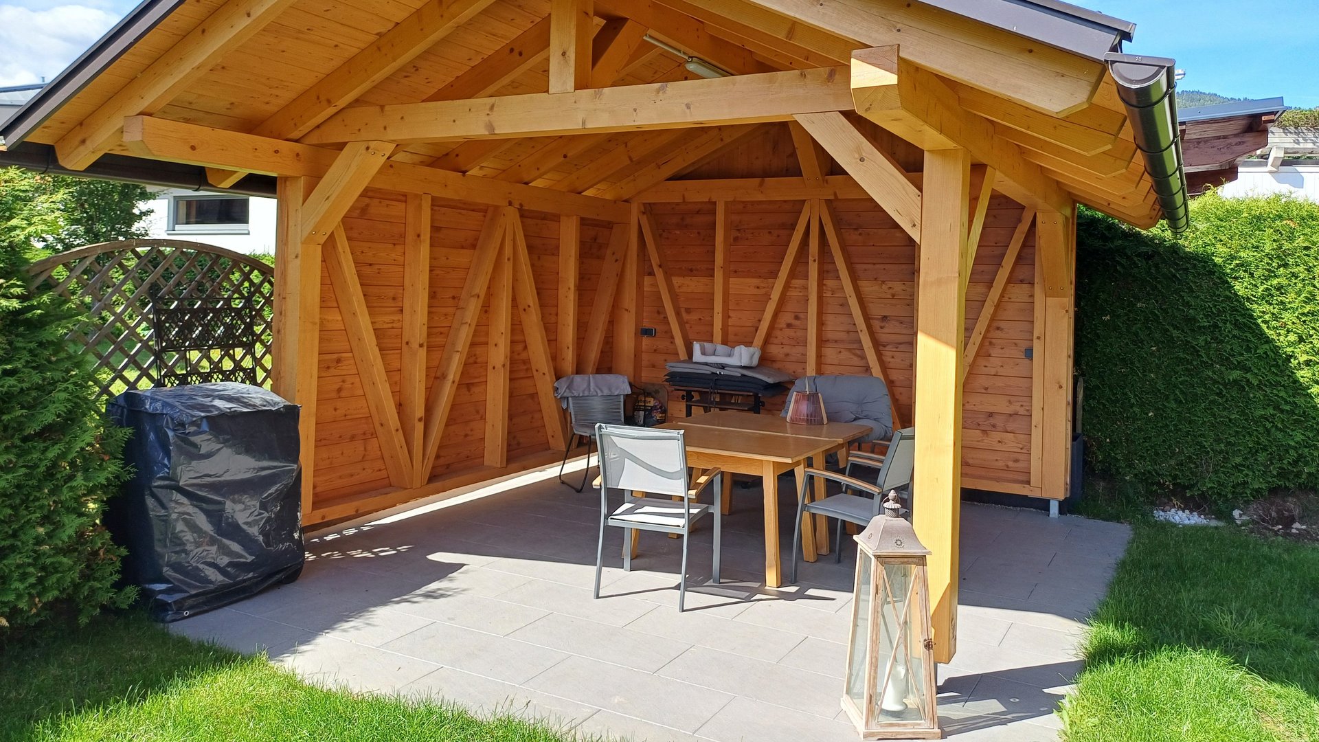 Charming wooden gazebo in a lush garden A wooden garden gazebo surrounded by outdoor furniture and well-kept grass lawn.