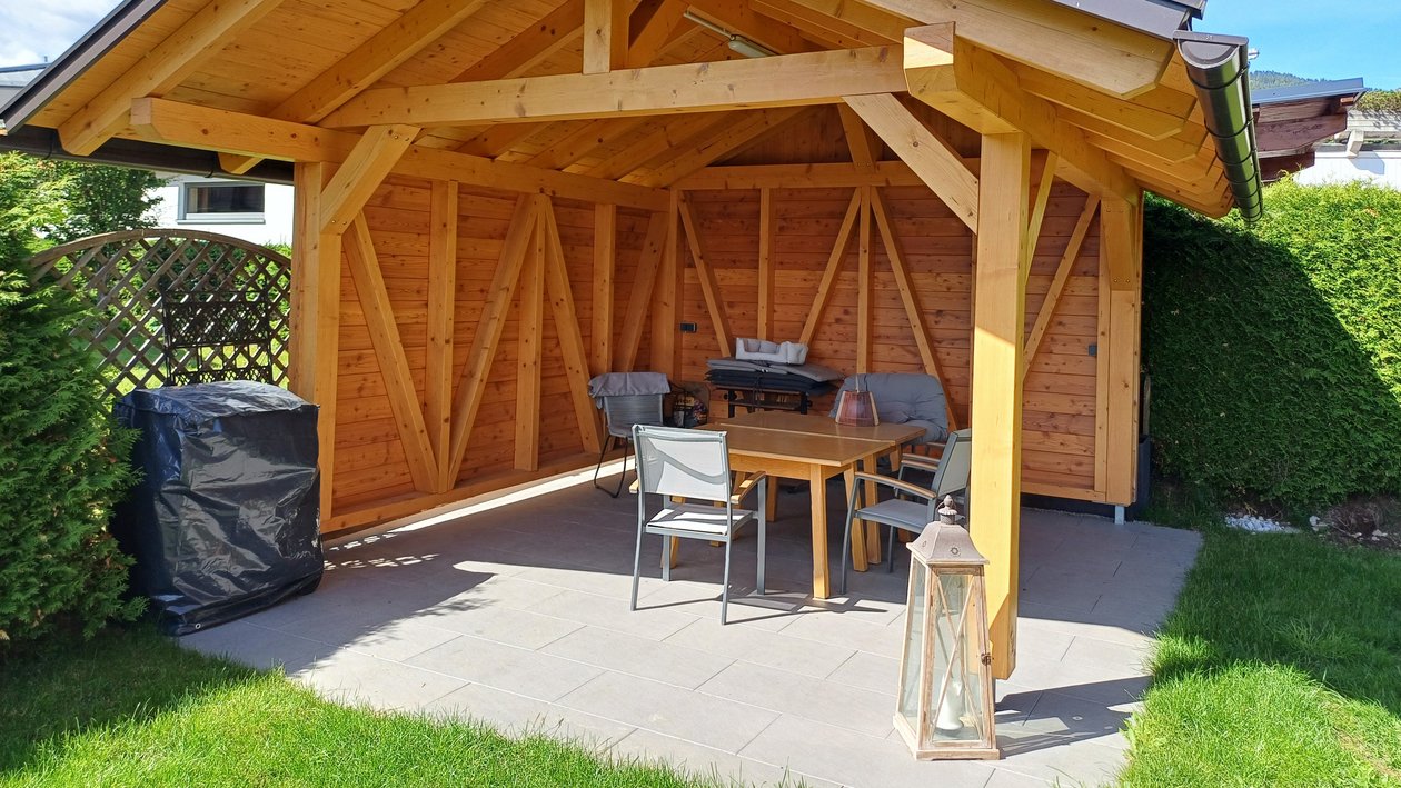 A wooden garden gazebo surrounded by outdoor furniture and well-kept grass lawn.