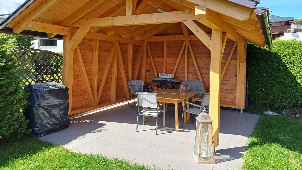 Eine Holzgartenlaube in einem gepflegten Garten mit Sitzmöbeln und Rasenfläche für Entspannung im Freien.