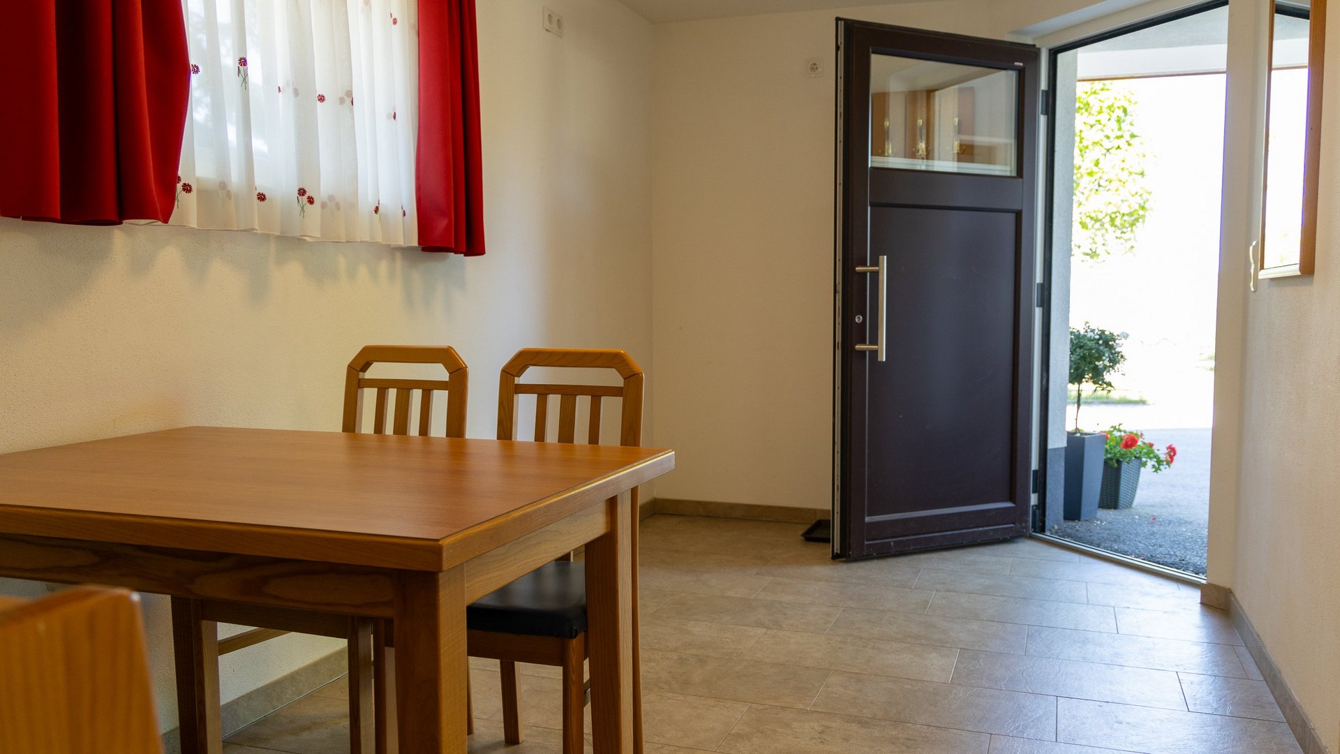 Ein schlichtes Interieur mit einem Holztisch, Stühlen, einem Fenster und einer offenen Tür