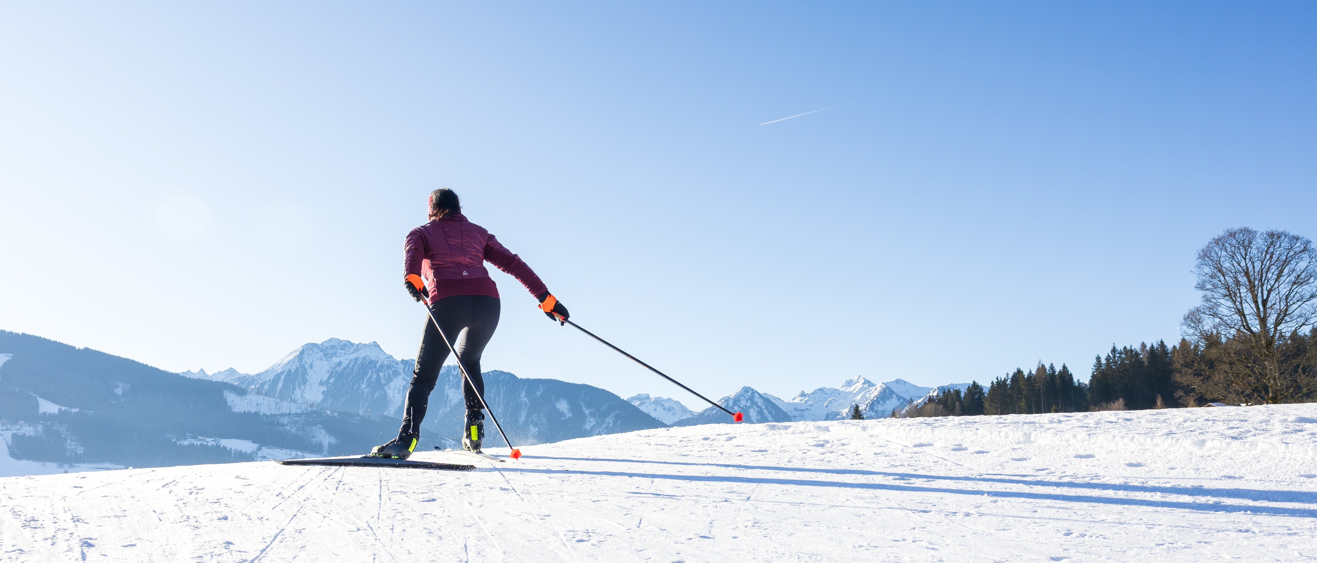 Person skiing on snow-covered landscape with mountains and blue sky in background