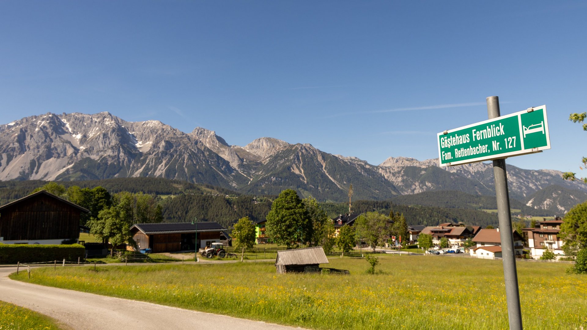 Grüner Wegweiser in einer ländlichen Umgebung mit Bergen im Hintergrund und weiten Feldern.