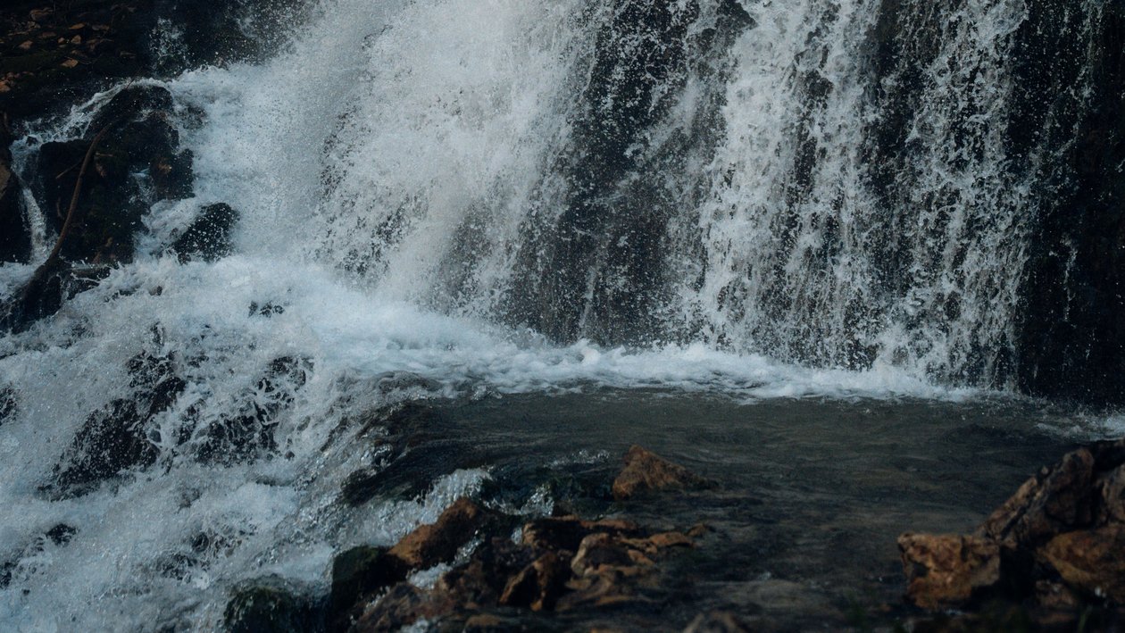 Cascading waterfall flowing over rocks surrounded by lush greenery and forested landscape