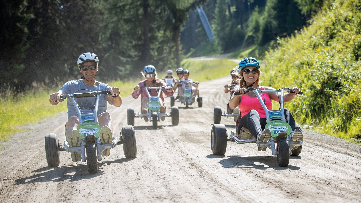 Gruppe von Personen fährt mit Go-Karts auf einem Schotterweg umgeben von Grünpflanzen