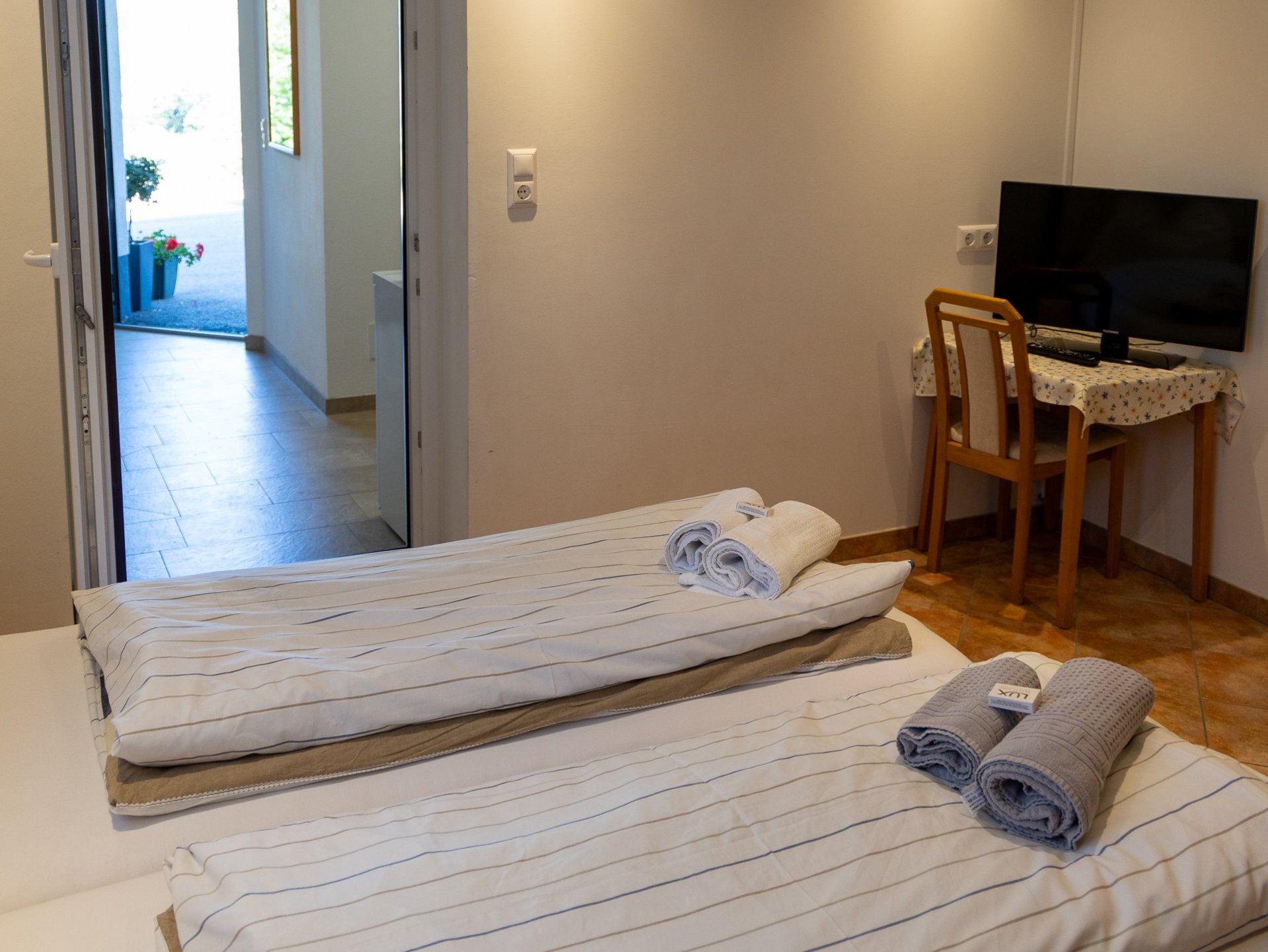 Hotelzimmer mit zwei Einzelbetten, Schreibtisch und Fernseher, Zugang zum Außenbereich