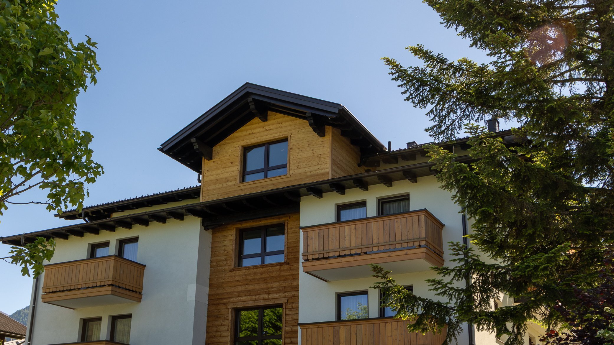 Multi-story residential building featuring a wooden exterior and balconies amidst trees