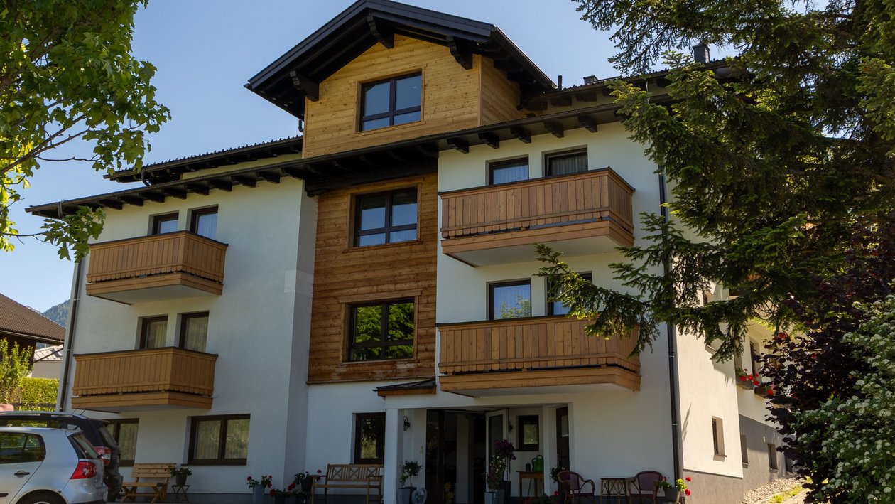 Mehrstöckiges Wohngebäude mit Holzbalcon und moderner Fassade inmitten von Grünflächen.