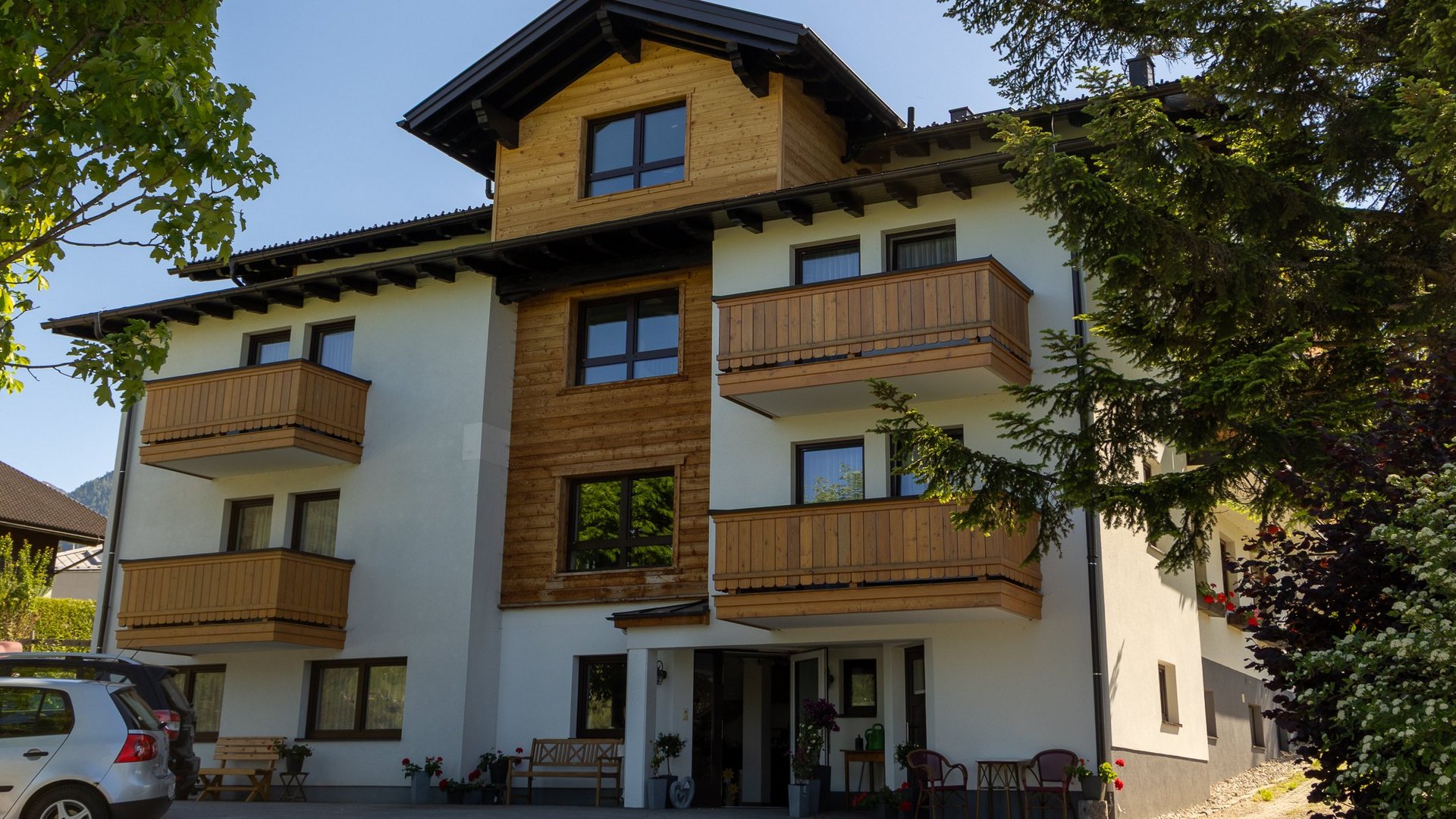 Mehrstöckiges Wohngebäude mit Holzbalcon und moderner Fassade inmitten von Grünflächen.
