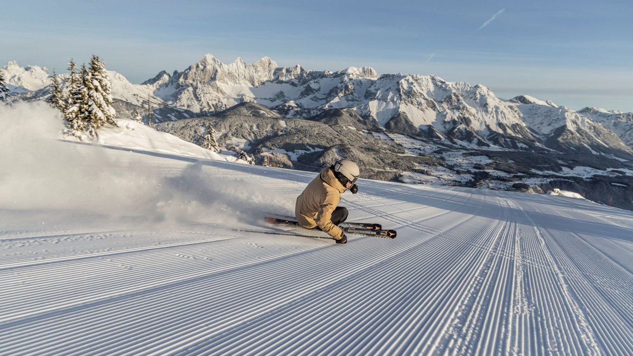 Skifahrer fährt durch frischen Schnee auf einem Berg mit schneebedeckten Gipfeln im Hintergrund