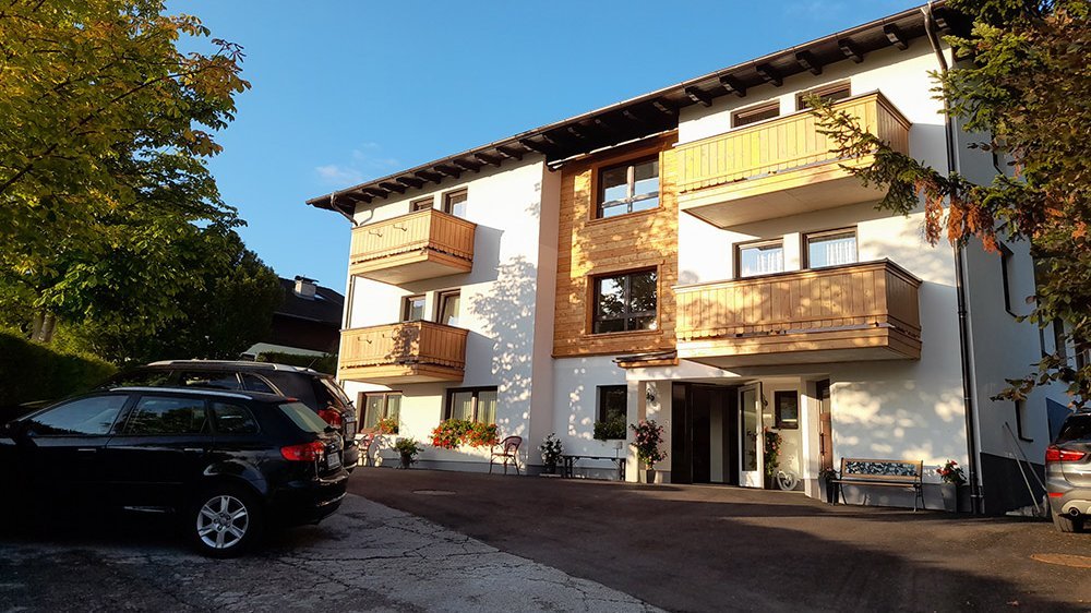 Modern residential architecture Three-story residential building with wooden balconies amidst green trees and blue sky