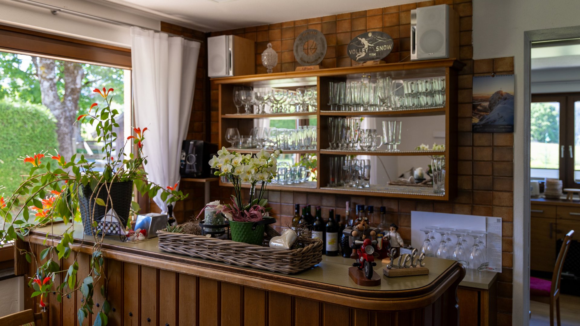 Gemütliche Homebar mit Holztheke, dekorativen Pflanzen und Glaswaren auf Regalen.