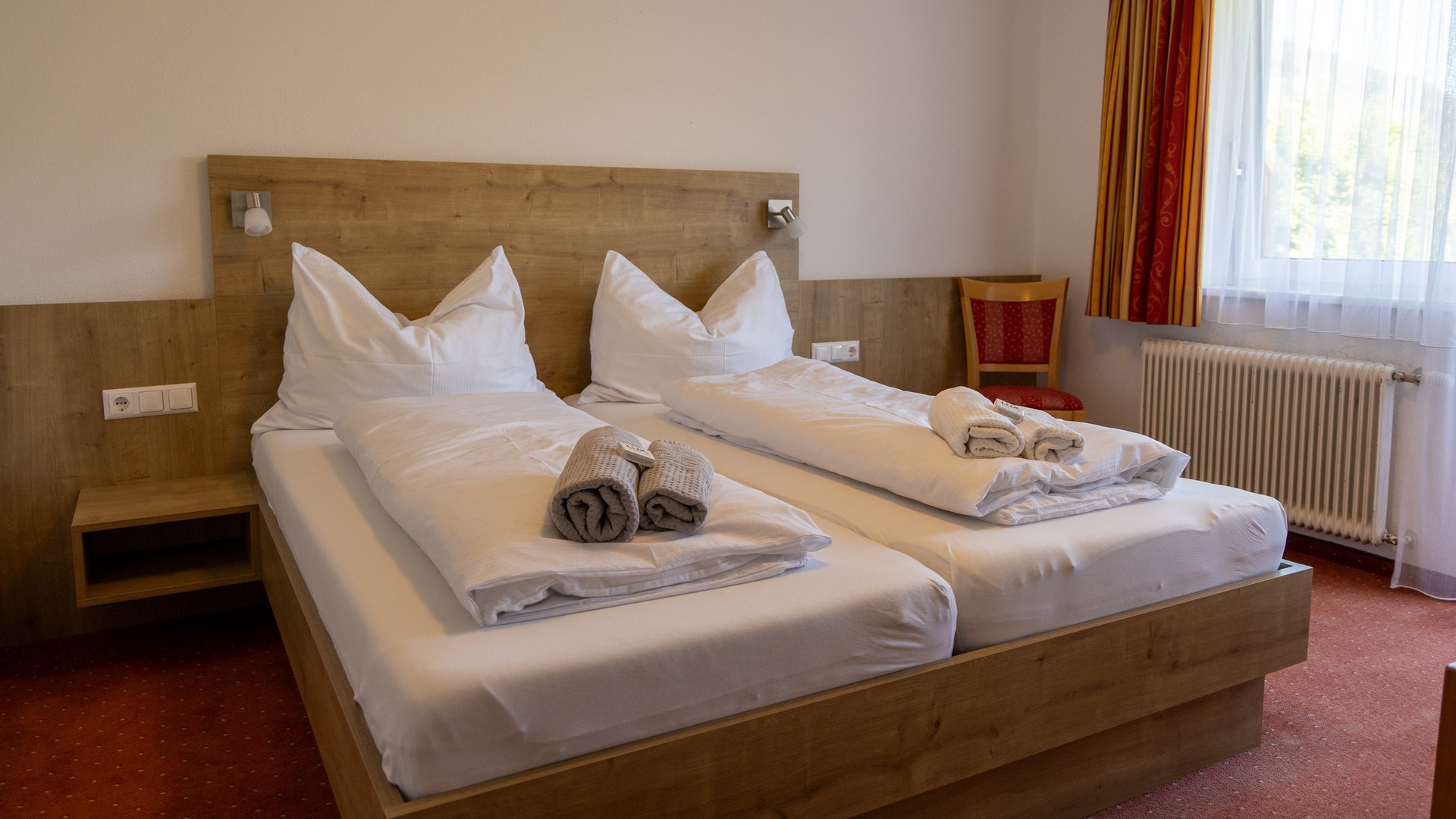 A hotel room with two single beds, white linens, decorative pillows, a wooden headboard, and a chair by the window.